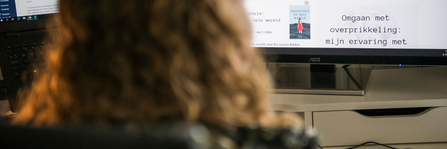 Foto van mij van de achterkant terwijl ik achter mijn computer zit. Je ziet onscherp mijn haar en scherp het scherm van mijn laptop en van mijn computer met daarop wat teksten van mijn blog.